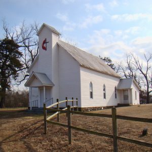 White church building with cross on central section and wooden fence