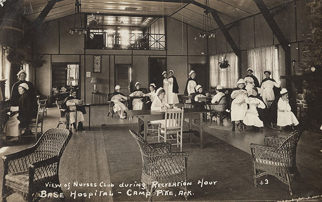 Group of white women in nursing uniforms socializing indoors in high-ceilinged room at "Base Hospital" at Camp Pike, Arkansas