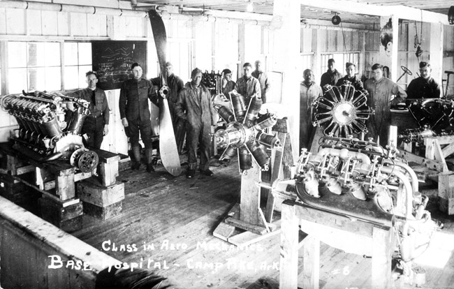 Class of young white men in machine shop posing with various aircraft engines