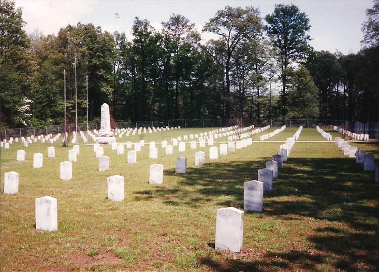 Rows of gravestones in cemetery with stone obelisk monument and flag poles in the background
