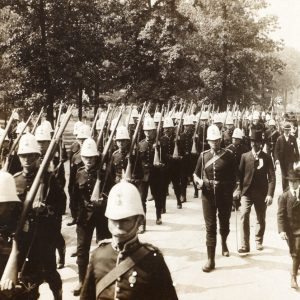 Men in helmets marching in parade with rifles over their shoulders