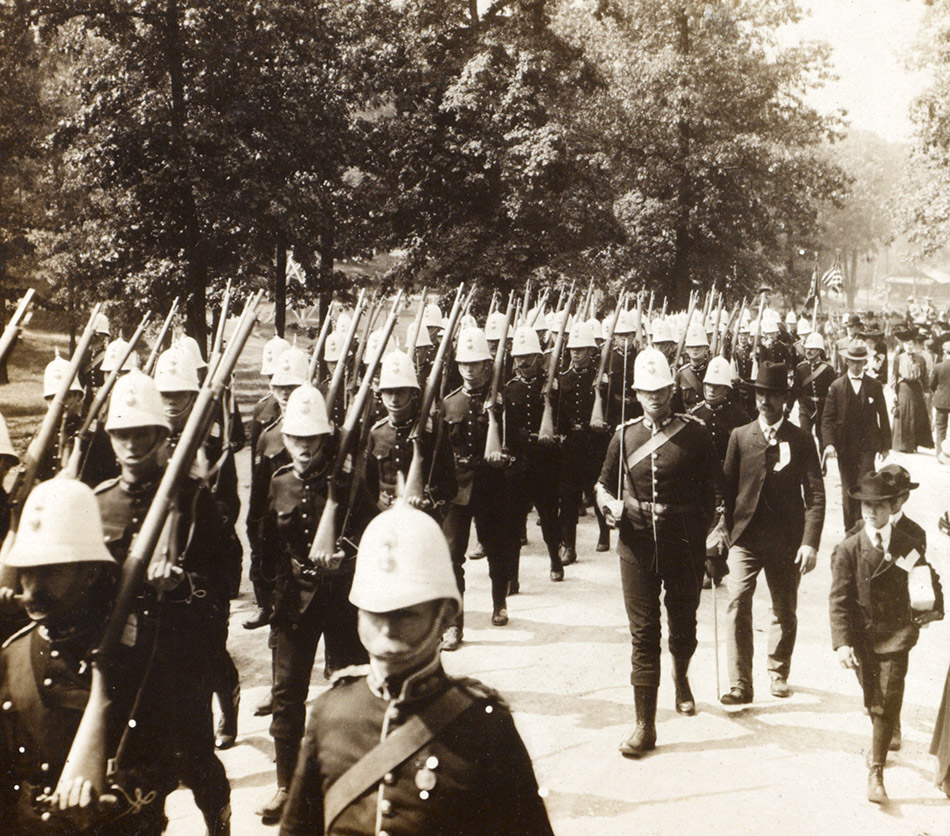 Men in helmets marching in parade with rifles over their shoulders