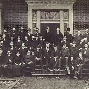 Group of white men in suits on steps of brick building