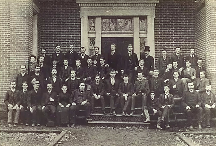 Group of white men in suits on steps of brick building