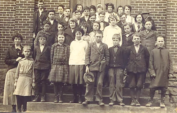 Group of white children and teachers on steps of brick building