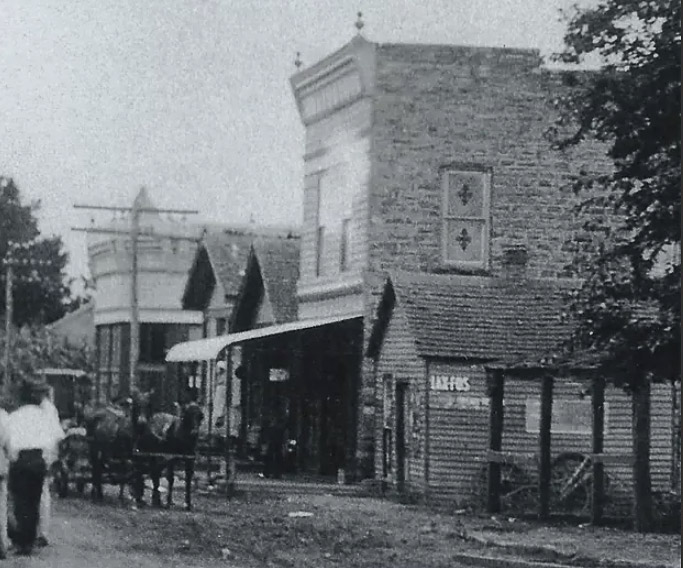 Horse-drawn carriage riding past brick storefronts on dirt road