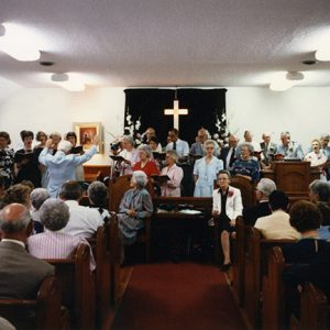 Men and women singing to congregation in church sanctuary with wooden pews and cross curtain