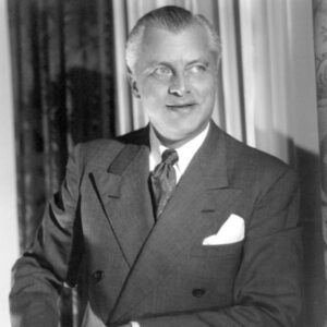 White man in suit and tie with curtains behind him