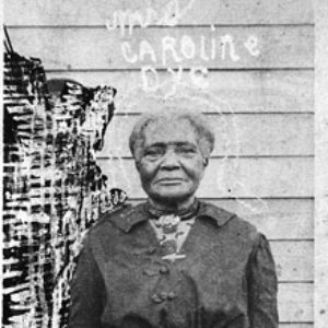Old African-American woman standing in dress outside building with wood siding