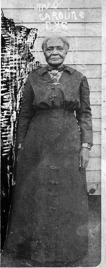 Old African-American woman standing in dress outside building with wood siding