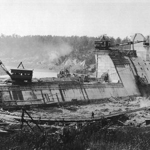 Concrete dam under construction with cranes and worker standing on bridge