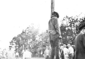Young African-American man hanging from a pole with white men in hats standing around him