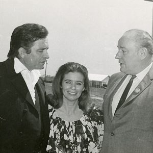 White man in black suit with white woman in floral dress talking to old white man in suit and tie