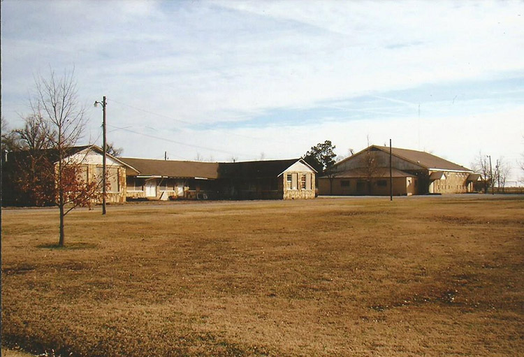 Single-story school building with two wings on grass and larger auditorium in background