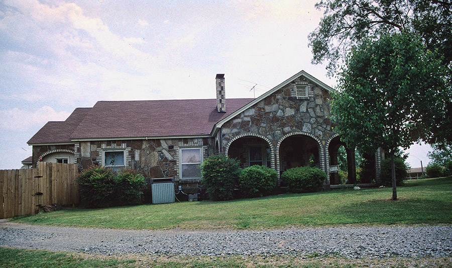 House with stone walls and three front arches with trees in front yard