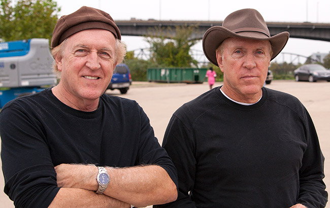 Two older twin white men wearing hats in matching black shirts