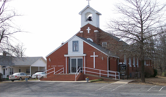 Brick church building with bell tower on parking lot with house next door