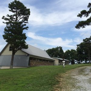 Side view of barn-shaped building and single-story building on gravel driveway