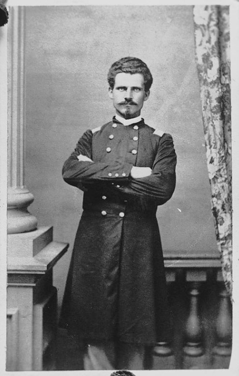 White man with mustache standing with arms crossed in military uniform