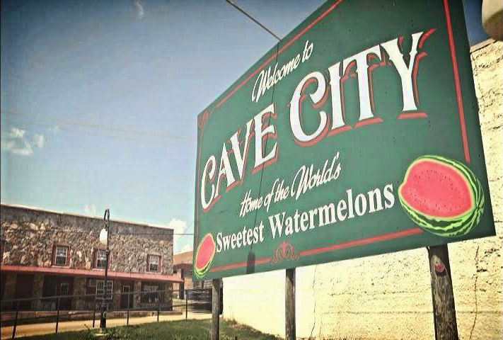 Multistory stone building with "Welcome to Cave City" sign in the foreground