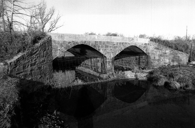 Stone arch bridge with concrete platform over creek