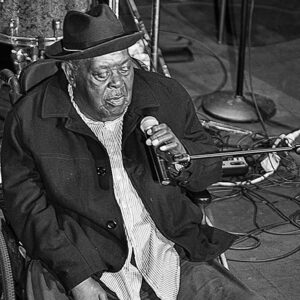 Older African-American man seated and singing into microphone on stage