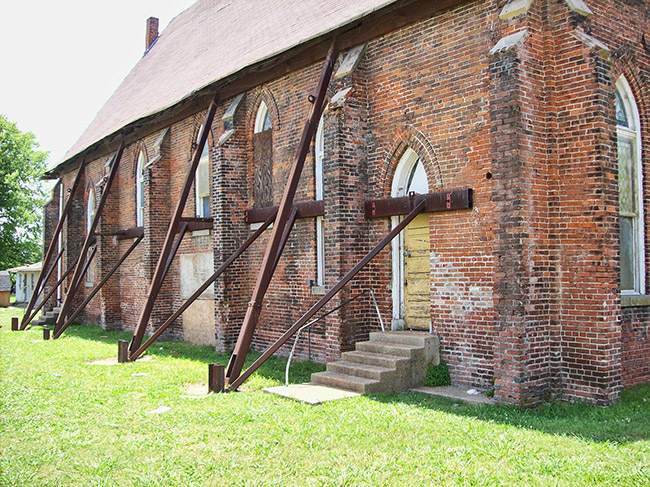Dilapidated brick church building with metal braces supporting the sides