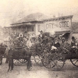 White men women and children on horse drawn wagons with storefronts behind them