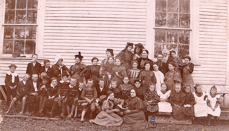 Group of white children and teachers outside school house