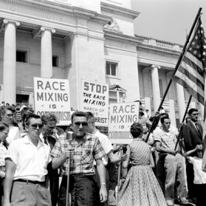 Crowd of white people with American flags and holding signs "Race Mixing is Communism" "Stop the Race Mixing March of the AntiChrist" on the capitol steps