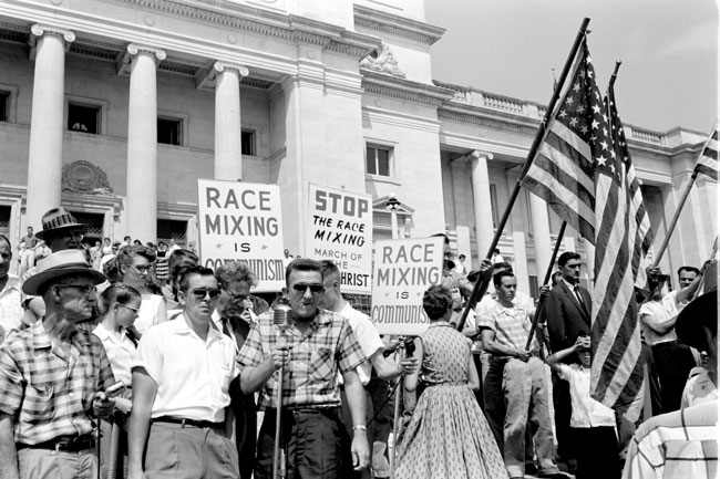 Crowd of white people with American flags and holding signs "Race Mixing is Communism" "Stop the Race Mixing March of the AntiChrist" on the capitol steps
