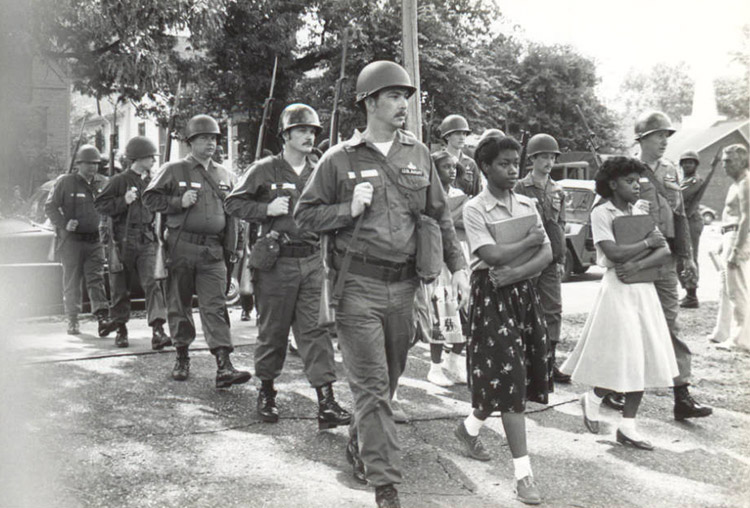 Pair of African-American girls in dresses being escorted by white men in military uniforms with guns and helmets