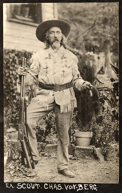 Old white man with long hair and beard in western clothing with hat and gun