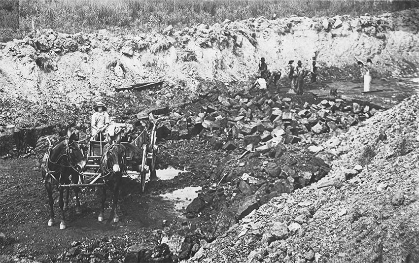 Man riding horse drawn buggy and other men at work in open pit mining area