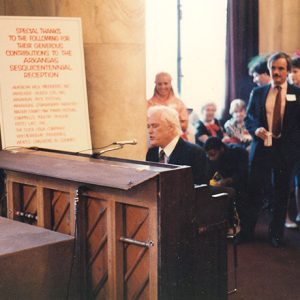 Old white man in suit playing piano and singing for a mixed crowd