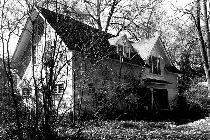 Two story house with boarded up windows in overgrown yard