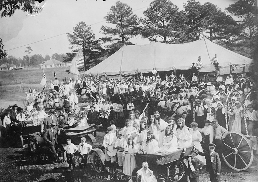 Large group of children and adults standing and seated in front of large tent