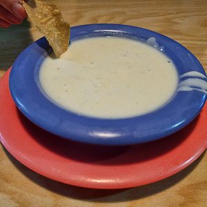 Dipping a chip in a blue bowl of cheese dip on a red plate