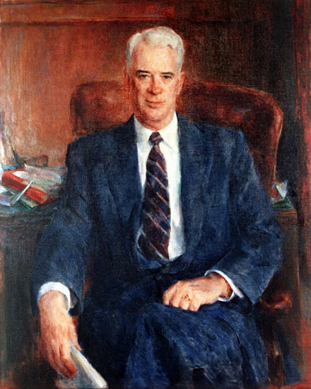 White man with in suit and tie sitting at his desk