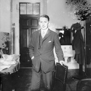 White man in suit standing at chair in office