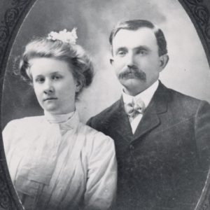 White man with mustache in suit and bow tie with white woman in dress