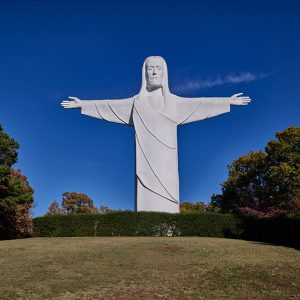 Gigantic boxy white Jesus statue with outstretched arms atop a hill