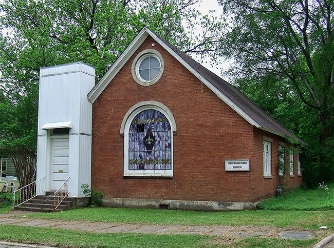Brick building with arched stained glass window and a white entrance addition on grass