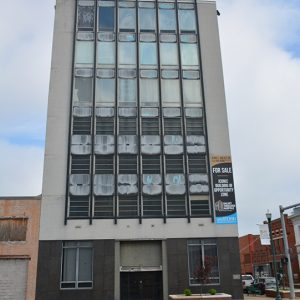 Tall multistory building with "For Sale" sign on its side on street corner