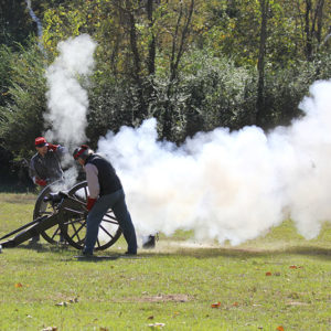 Group of white men in period costume firing a cannon in a field