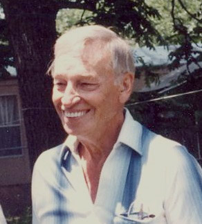 Older white man smiling in collared shirt with house and tree behind him