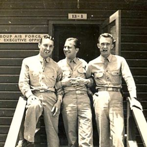 Three smiling white men in military uniform standing casually outside office executive building