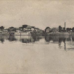 View from across river of town buildings and steamboat floating alongside the shore