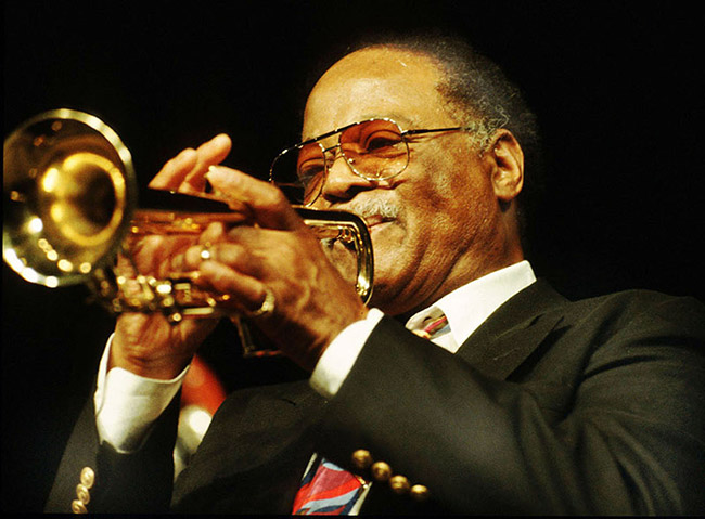 African-American man in suit with glasses playing a trumpet