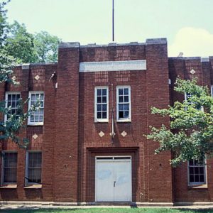 Close-up of two-story brick building with flag pole on street